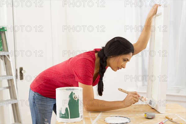 Mixed race woman painting window pane