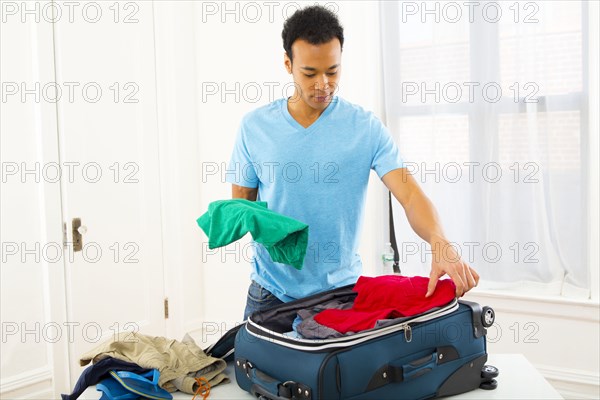 Mixed race man packing suitcase