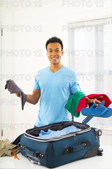 Mixed race man packing suitcase