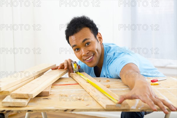 Mixed race carpenter measuring wood with tape measure