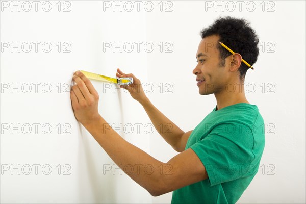 Mixed race man measuring wall