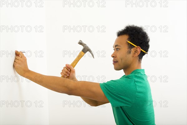 Mixed race man hammering nail into wall