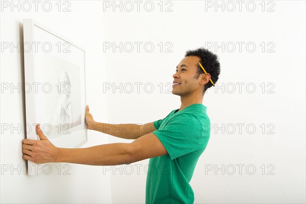 Mixed race man hanging picture on wall