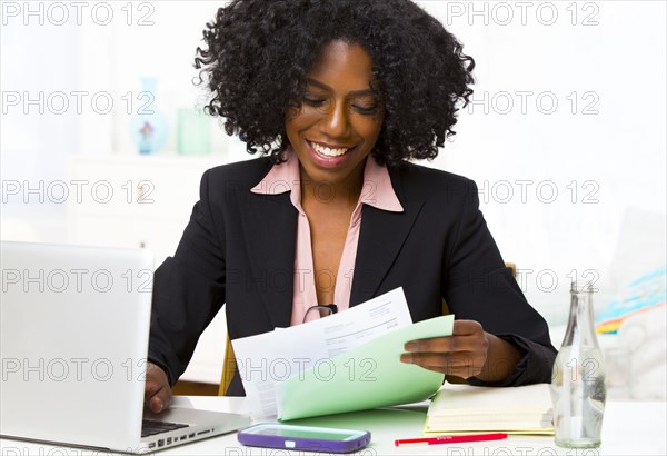 Mixed race businesswoman reading papers at desk