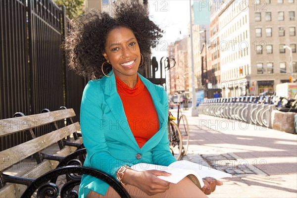 Mixed race woman reading on city bench