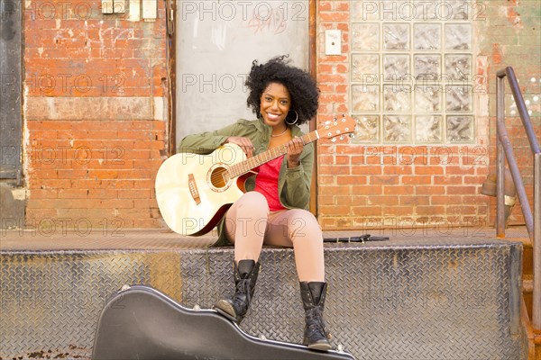 Mixed race woman playing guitar in city