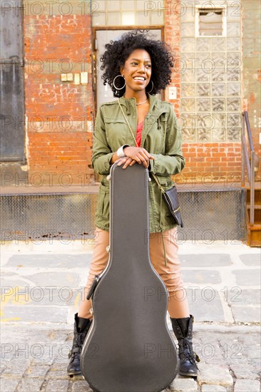 Mixed race woman with guitar case on city street