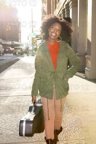 Mixed race woman carrying guitar case on city sidewalk