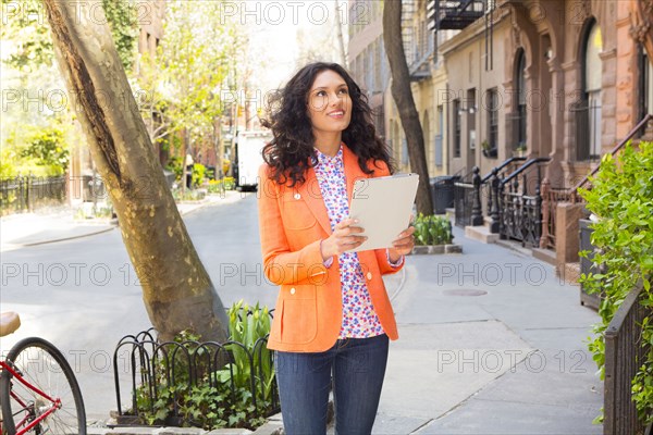 Mixed race woman using tablet computer on city sidewalk