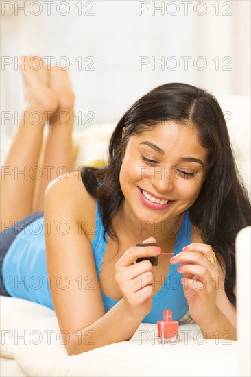 Hispanic woman painting her nails on sofa