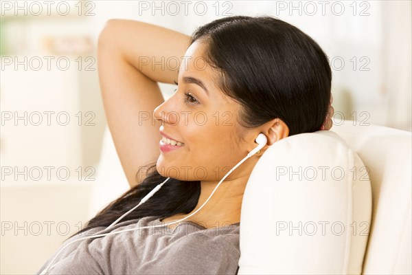 Hispanic woman listening to earphones on sofa