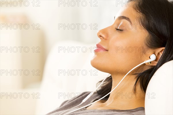 Hispanic woman listening to earphones on sofa