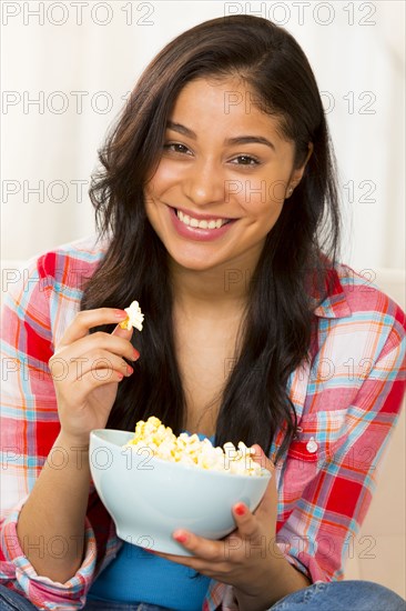 Hispanic woman eating popcorn on sofa