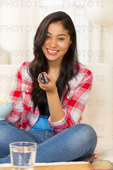 Hispanic woman watching television on sofa