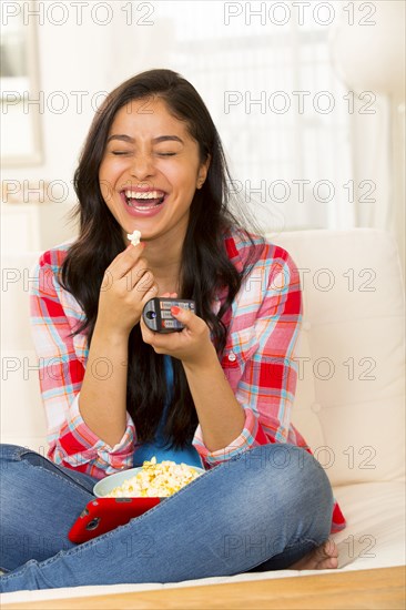 Hispanic woman eating popcorn on sofa