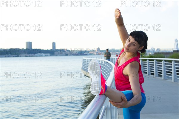 Mixed race woman stretching on urban waterfront railing