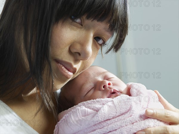 Mixed race mother cuddling newborn baby