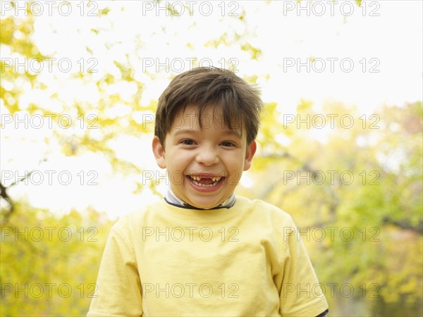 Toothless Hispanic boy grinning outdoors in autumn