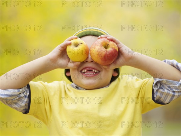 Toothless Hispanic boy covering eyes with apples