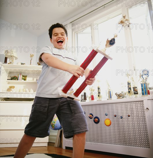 Happy Hispanic boy holding trophy in bedroom