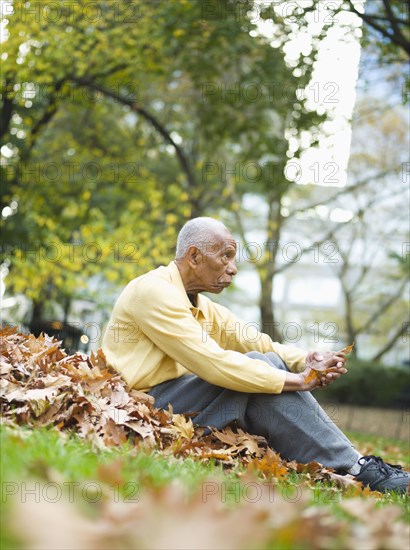 Senior man sits in autumn leaves in park