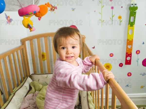 Mixed race baby girl standing in crib