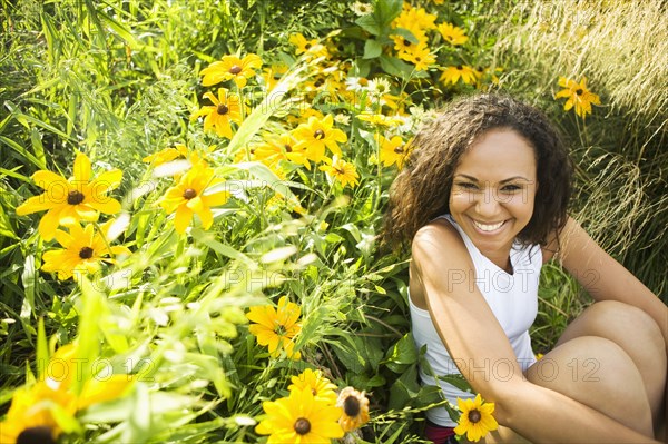 Smiling Hispanic woman sitting in field of flowers