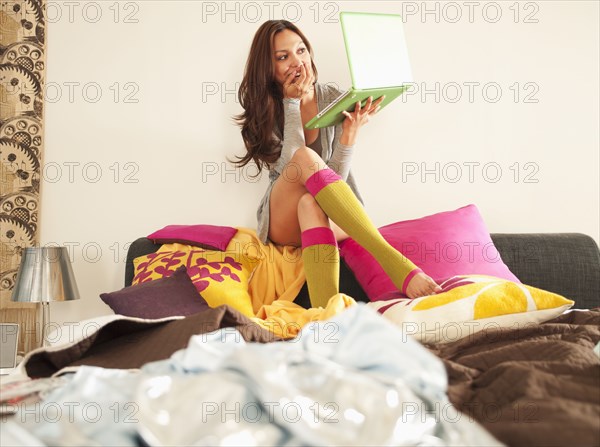 Hispanic woman using laptop on bed