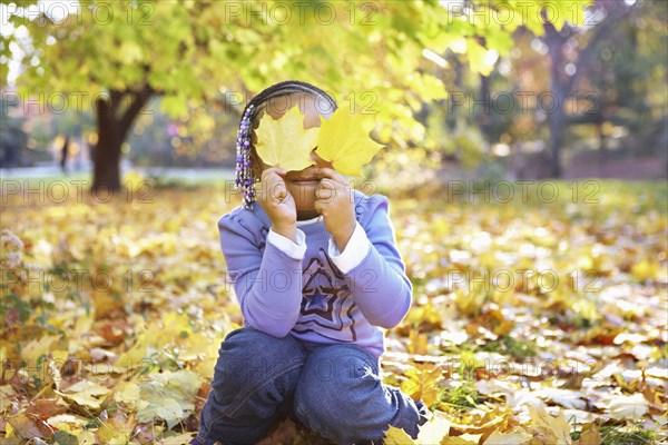 Mixed race girl holding autumn leaves over her eyes