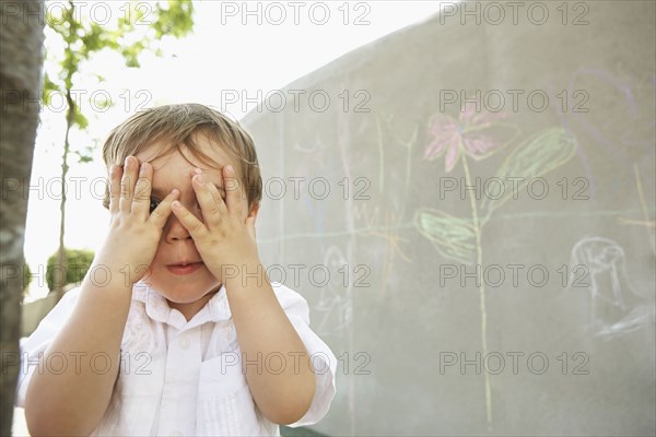 Mixed race boy covering his eyes outdoors