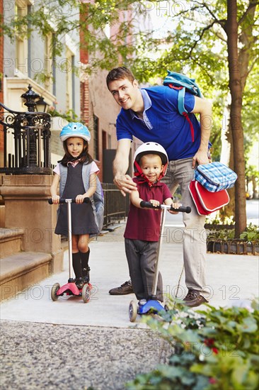 Father taking children on scooters to school