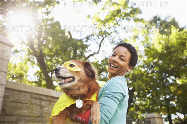 Black woman carrying costumed dog in park