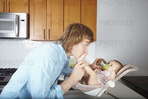 Father kissing baby's feet in chair