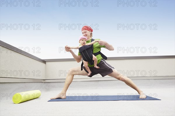 Father practicing yoga and holding baby