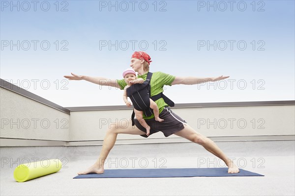 Father practicing yoga and holding baby