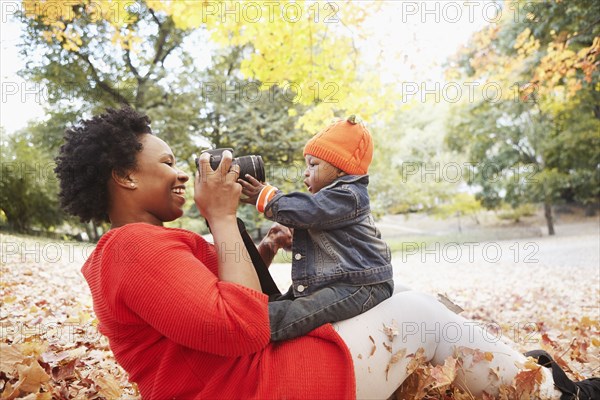 Black mother taking pictures of toddler son in park