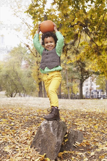 Mixed race boy holding pumpkin overhead in park