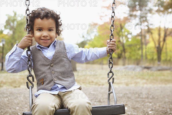 Mixed race boy sitting on swing in park