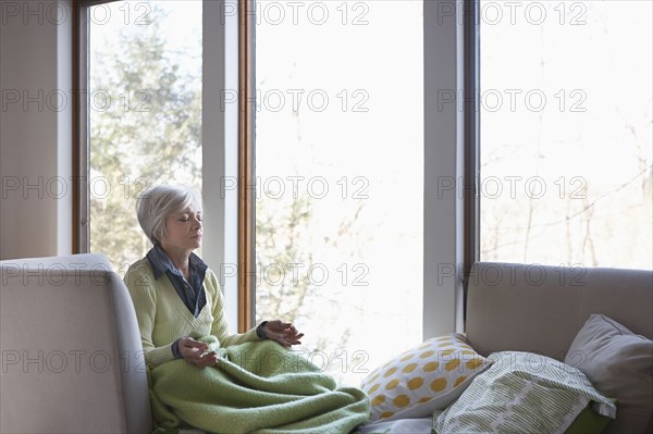 Senior woman meditating on sofa