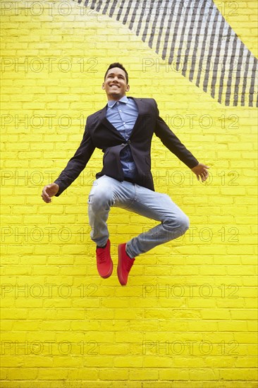 Smiling man jumping for joy near bright yellow wall