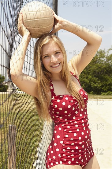 Smiling woman holding volleyball near net on beach