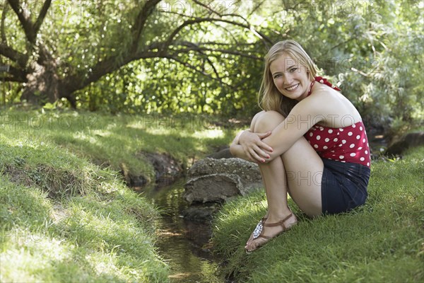 Smiling woman sitting near creek in park