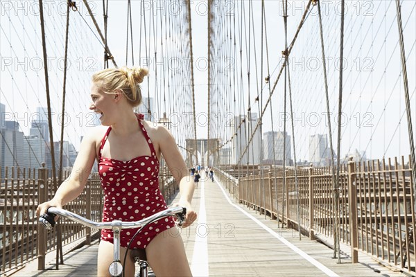 Smiling woman riding bicycle across urban bridge