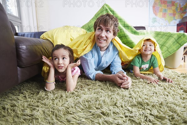 Father and children playing in blanket fort in living room