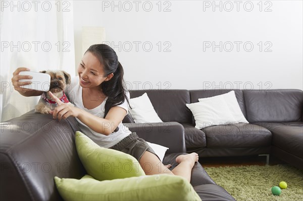 Chinese woman taking cell phone selfie with dog in living room