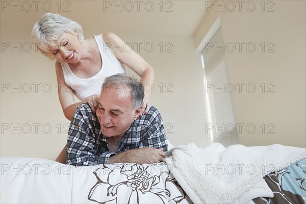 Older woman giving husband back massage on bed