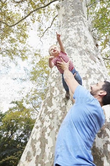 Caucasian father lifting baby son under tree