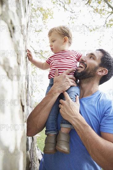 Caucasian father holding baby son under tree