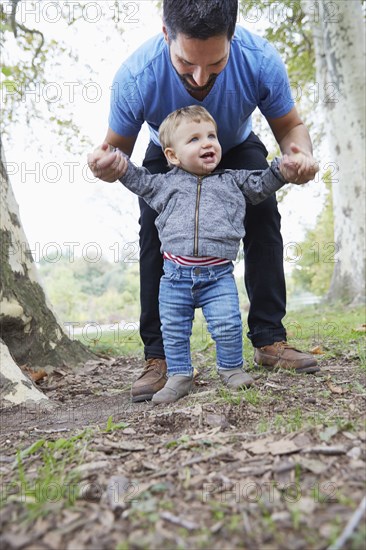 Caucasian father helping baby son walk outdoors