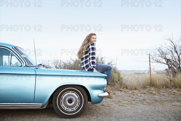 Smiling woman sitting on vintage car